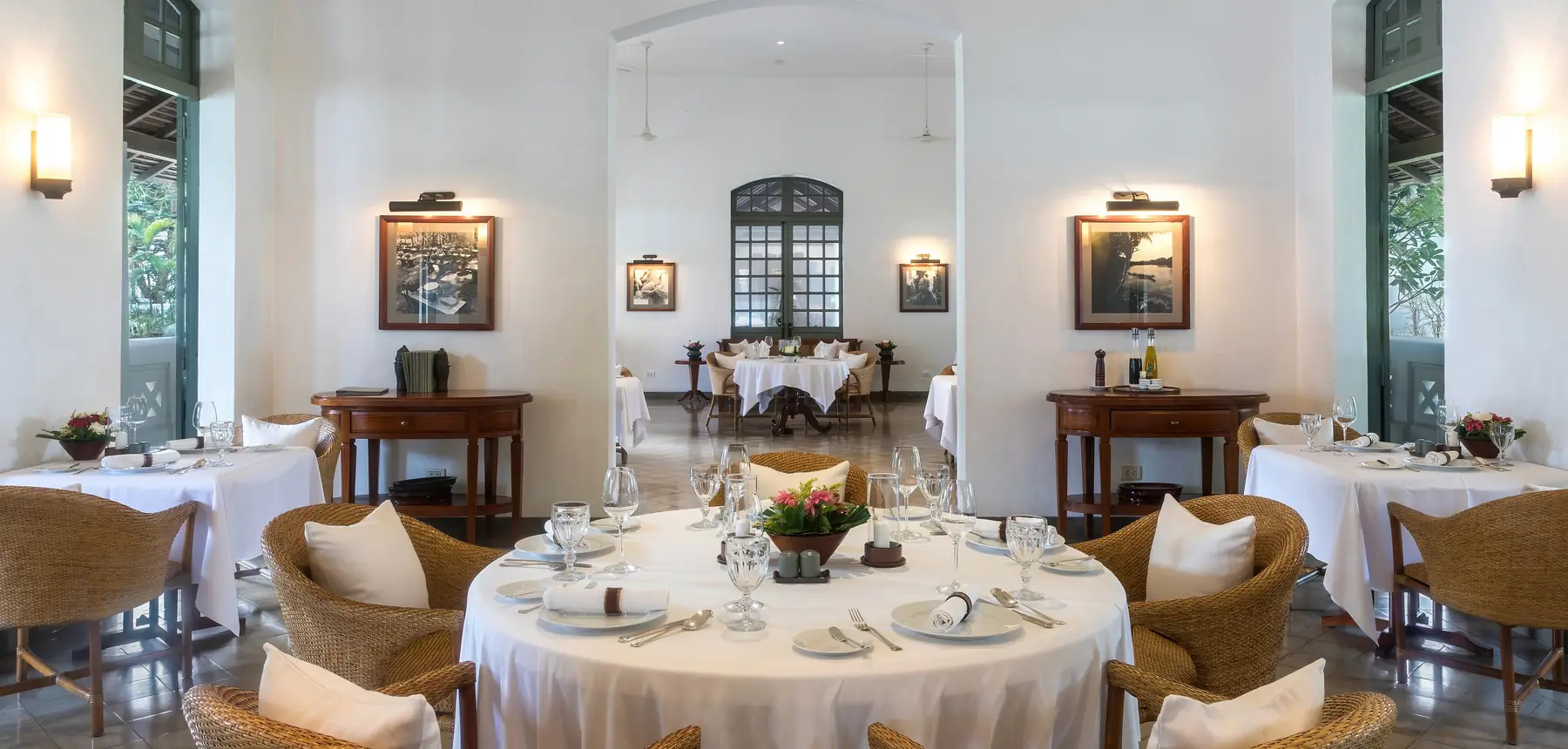 Dining room set with white linen, glassware and cane armchairs