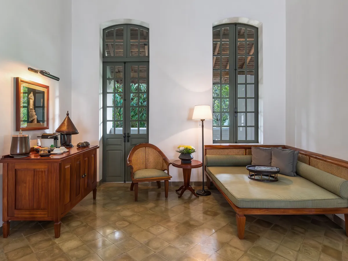 Sitting area of a resort suite with a daybed, writing cabinet and tall shuttered windows